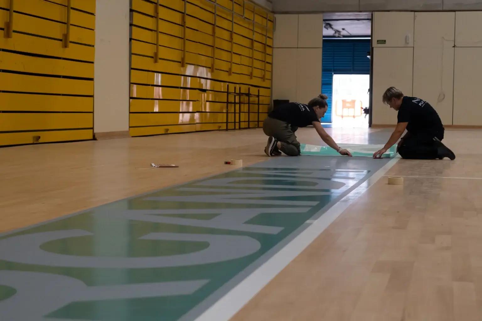 Equipo de Neolaser instalando la gráfica de Arganda del Rey sobre el parqué de la pista